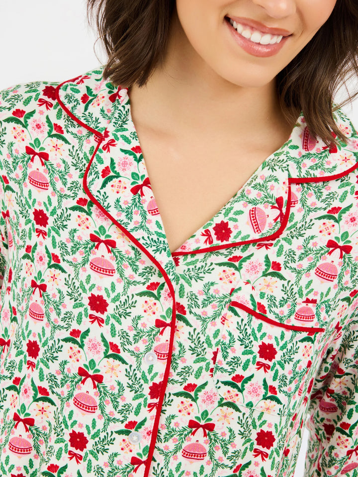Charlotte Trimmed with Joy Pants Set: button-up pajama top in a white print of red poinsettias, green foliage, and Christmas ornaments with red piping.