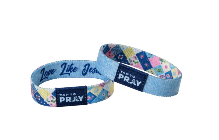 Two Tap To Pray™ Wristbands in patchwork blue quilted pattern, one reading “Love Like Jesus” with navy tags.