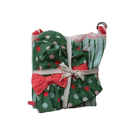 Folded Mrs Claus child apron with green, red, and light blue polka dot pattern, red bow, and pom-pom trim.