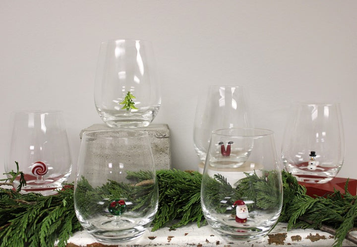 Set of six clear stemless wineglasses with decorative Christmas icons inside the base.