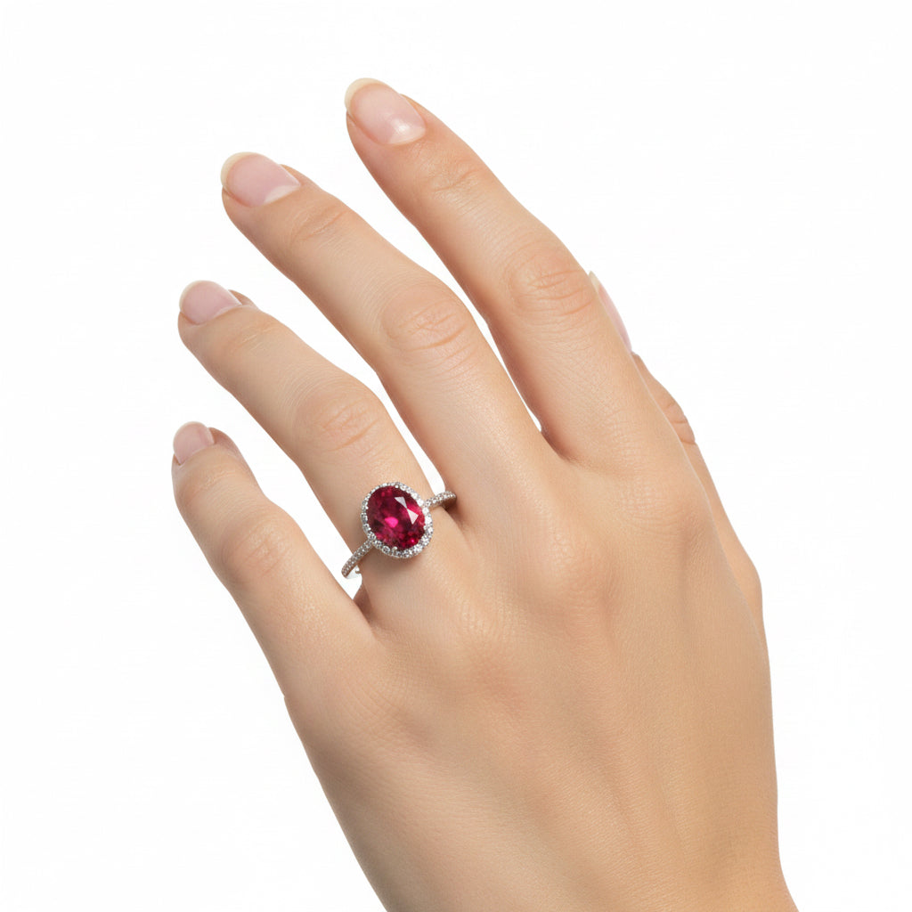 The Ring Edit: silver ring with large oval red gemstone, surrounded by small clear stones. Available in sizes 5-9.