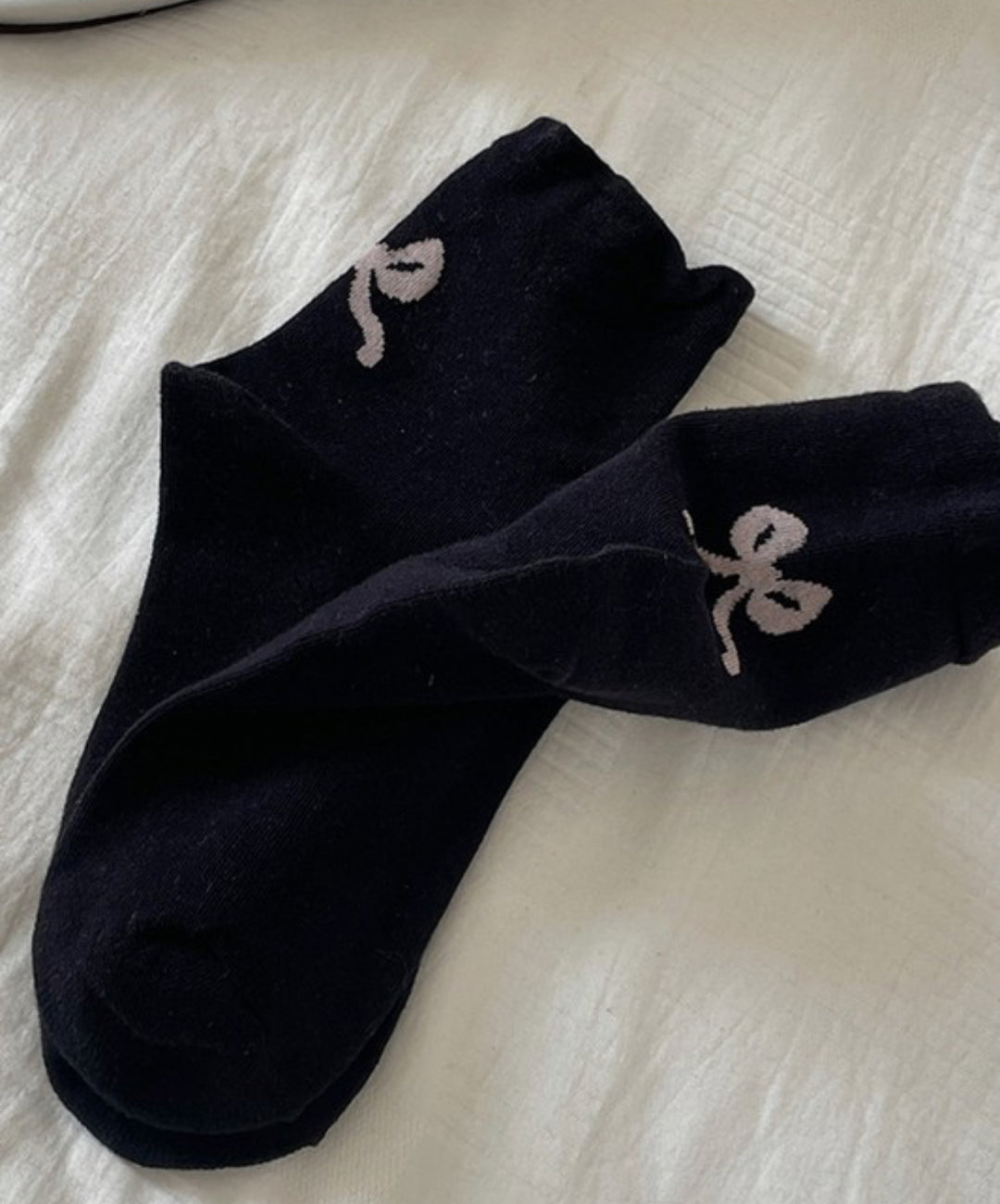 These Bow Mid-Calf Socks are adorned with white embroidery featuring abstract figures. The socks reach up to mid-calf length and have a unique, eye-catching design. They are available in one size that fits all.