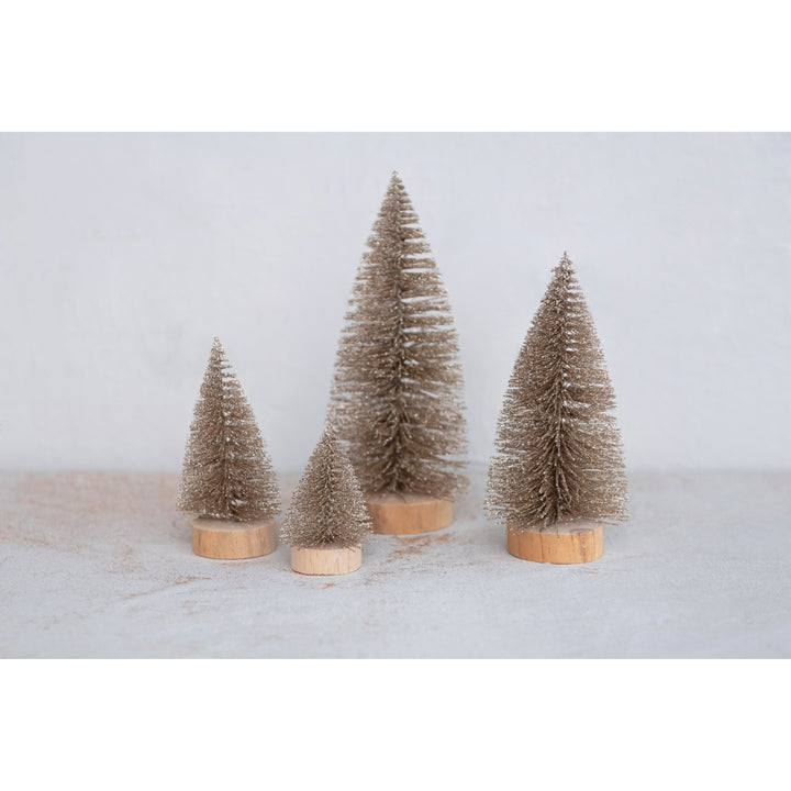 Four miniature champagne-colored bottle brush trees on wooden bases.