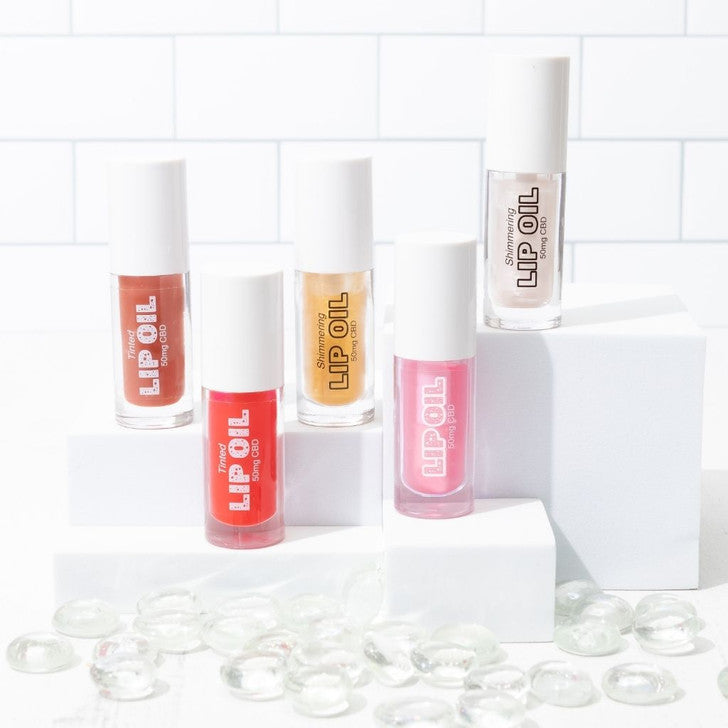 Tinted Lip Oil in red, pink, gold, clear, and peach shades. Available in 10ml and 15ml sizes. Set of five bottles shown.