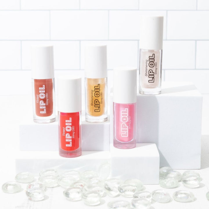 Tinted Lip Oil in red, pink, gold, clear, and peach shades. Available in 10ml and 15ml sizes. Set of five bottles shown.