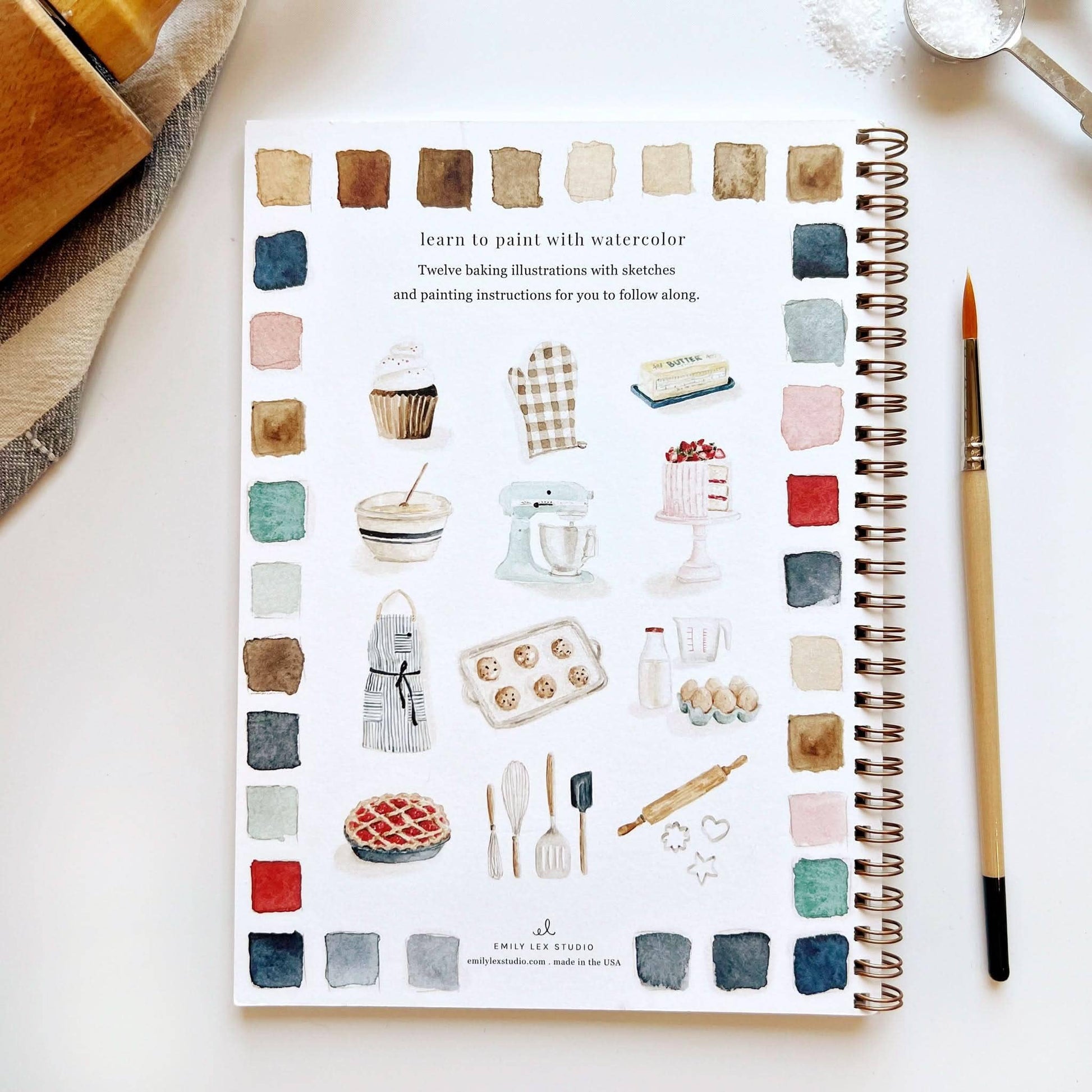 The Baking Watercolor Workbook is a spiral-bound painting book with illustrations of baked goods, kitchen tools, and a paintbrush. Available in standard size.