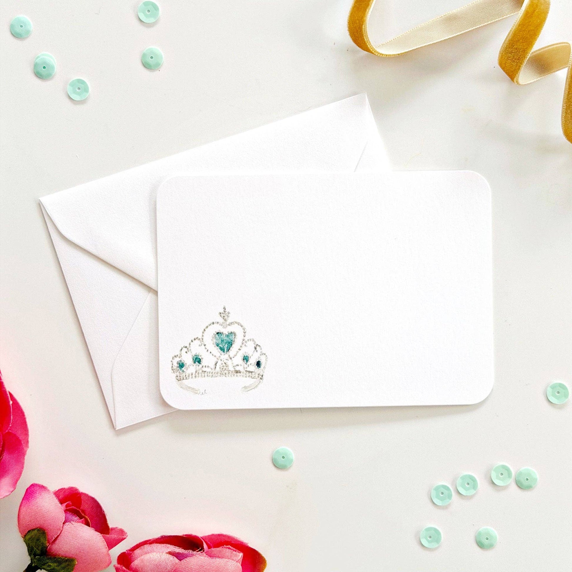 White notecard and envelope with tiara, pink flowers, sequins, and gold ribbon. Available in 4x6" and 5x7" sizes.