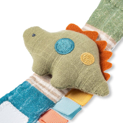 A colorful Itzy Bitzy Wrist Rattle: Dino with patchwork design, featuring blue, green, and orange natural cotton fabrics, lying on a white background.
