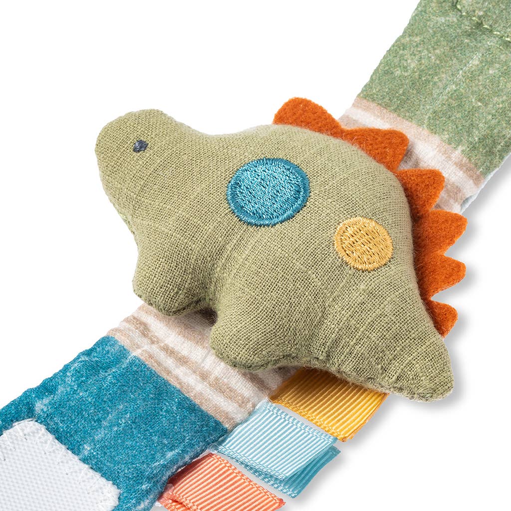 A colorful handmade Itzy Bitzy Wrist Rattle: Cottage featuring a green body with blue, orange, and yellow patchwork details and orange spiky ridges made from natural cotton fabric, displayed against a white background.