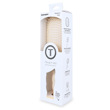 White rectangular box with clear window shows a tan Detangler Hair Brush for medium hair; simple illustrations and instructions on the side. Available in size for medium hair.