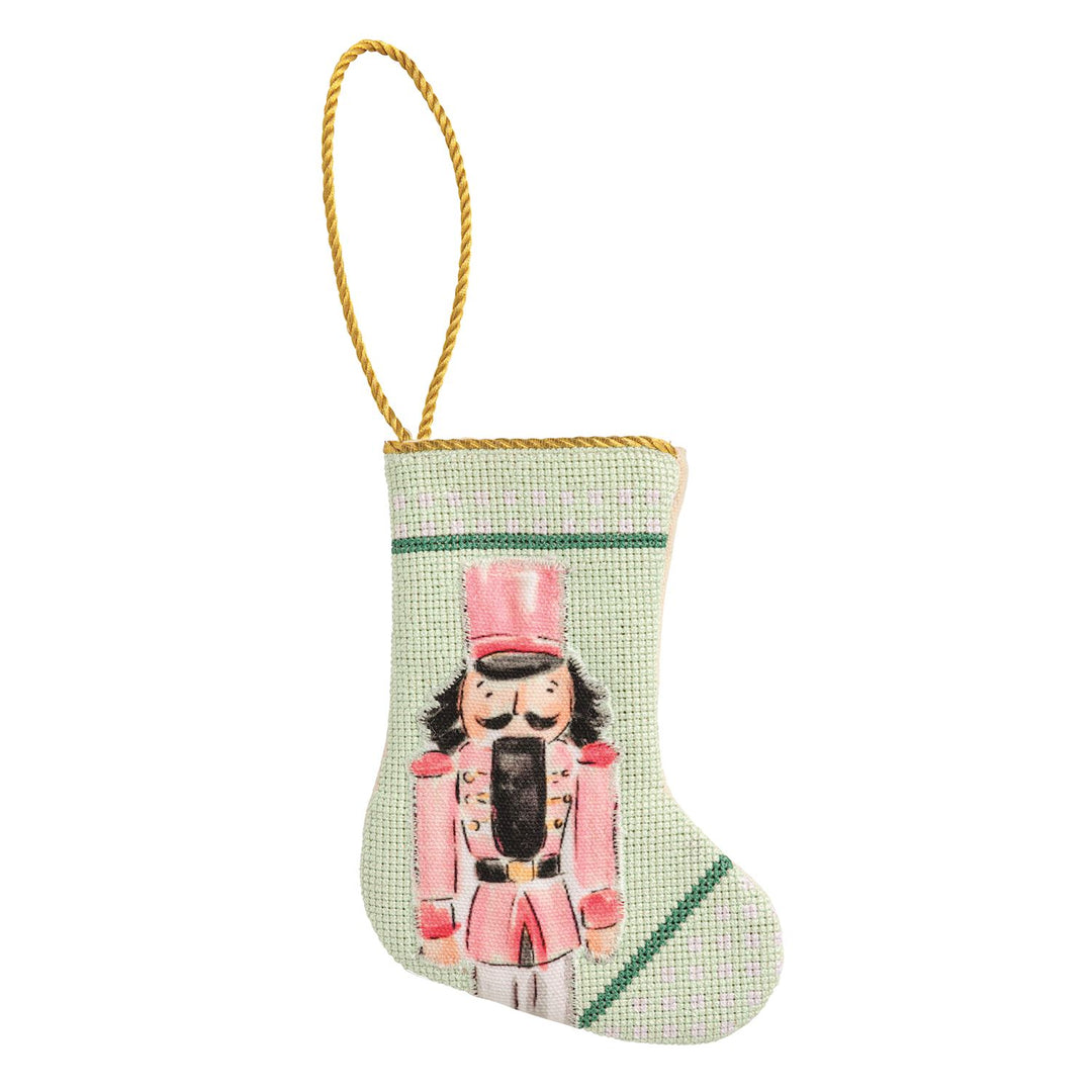 Pale green needlepoint nutcracker mini stocking with pink nutcracker design and gold hanging loop.