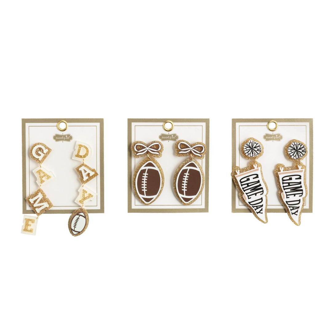 Tailgate Earrings | 3 Styles set includes three pairs: one with “GAME DAY” letters and a football, one with footballs and bows, and one with “GAME DAY” pennants plus pom-poms. Each pair comes on a display card. Sizes available: not specified.