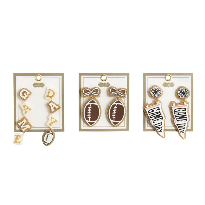 Tailgate Earrings | 3 Styles set includes three pairs: one with “GAME DAY” letters and a football, one with footballs and bows, and one with “GAME DAY” pennants plus pom-poms. Each pair comes on a display card. Sizes available: not specified.