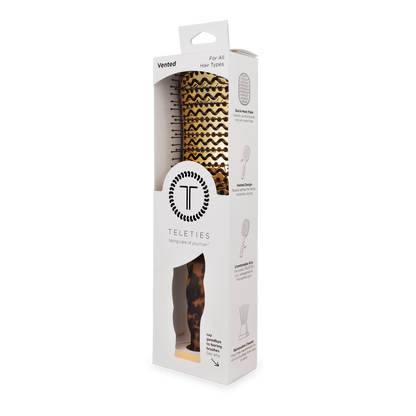 Boxed Vented Hair Brush | Tortoise by TELETIES, featuring a brown and gold chevron pattern, suitable for all hair types. Includes quick-heat aluminum plate for smooth blowouts. Primarily white packaging with product details and feature illustrations. Sizes available: standard and mini.