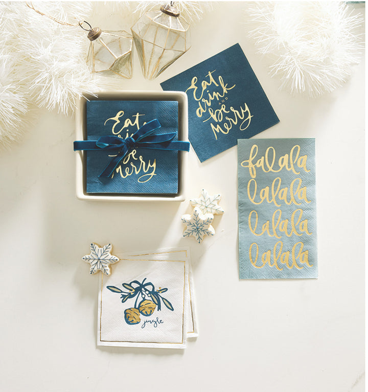 Square navy and white cocktail napkins with gold foil “Eat, drink and be merry,” “falala,” and jingle bell designs.