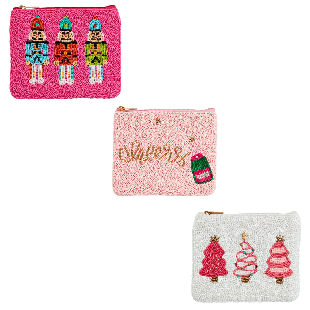 Three rectangular Holiday Beaded Cases: one hot pink with nutcrackers, one light pink with “cheers” and a champagne bottle, and one white with stylized Christmas trees.