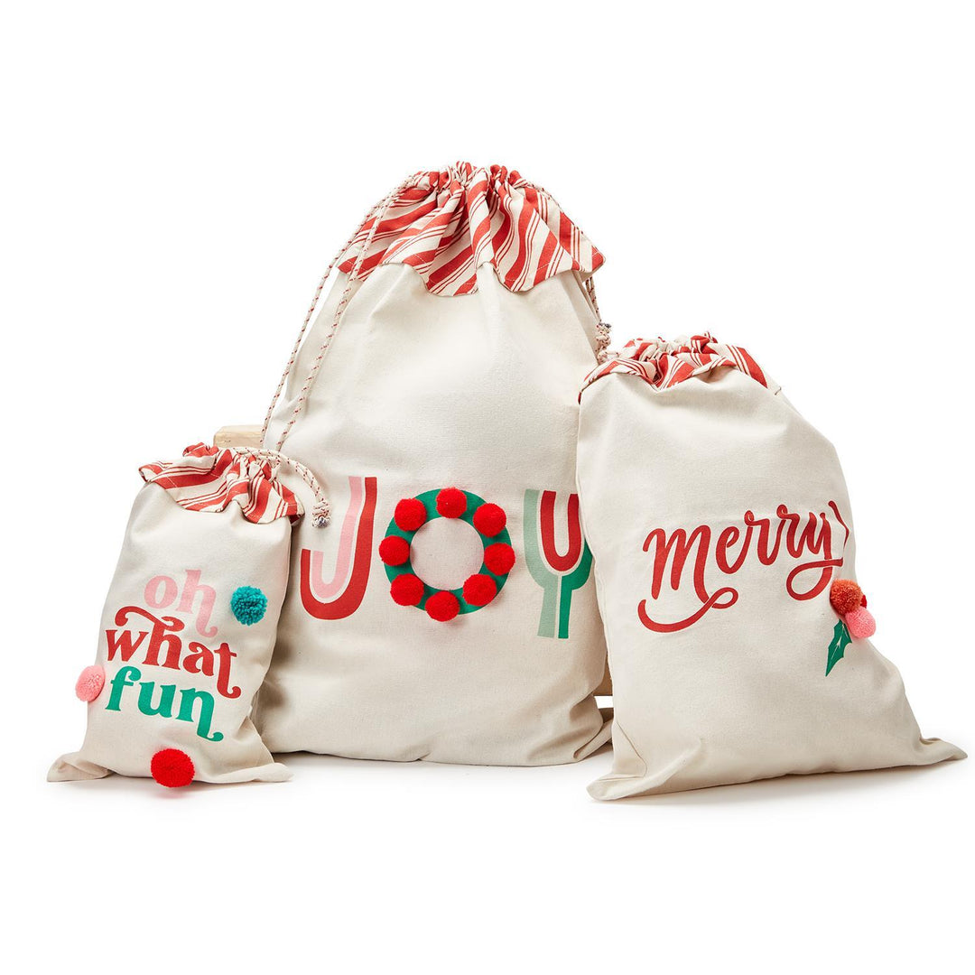 Three holiday reusable gift bags in varying off-white sizes, each with a red-and-white striped drawstring top and festive holiday lettering and embellishments.