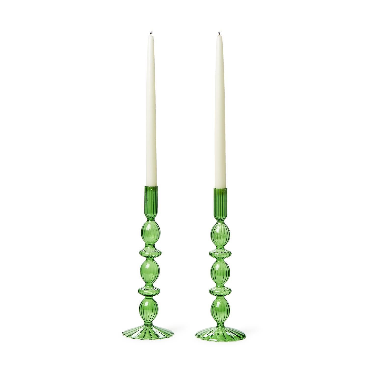 Two tall white candles in hand-blown glass candlesticks with ornate green holders, featuring a spherical ribbed design for elegance and stability.