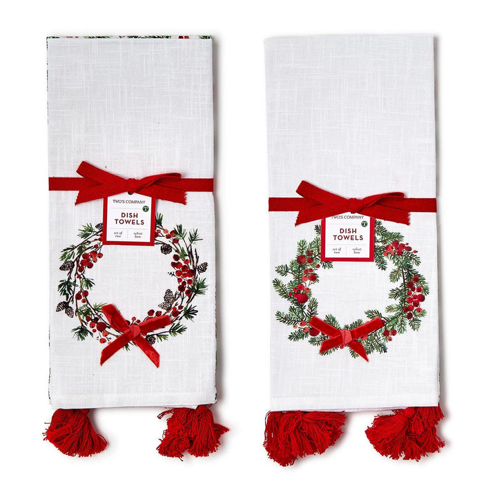 Merry Berry set of 2 white dish towels featuring a holiday wreath pattern of pine branches, pinecones, and red berries, accented with red velvet bows and tassels.