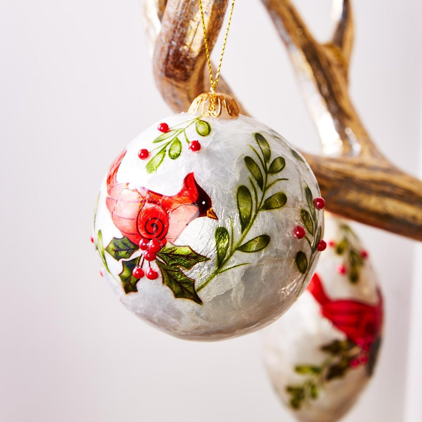 Hand-Painted Capiz Shell Cardinal Ornaments feature a red cardinal with green leaves and red berries. Available in one size.