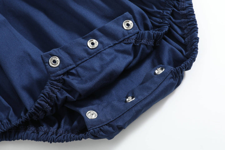 Close-up of snap button closure on dark blue elastic fabric of the Blue Nativity Smocked Ruffle Romper, available in size 6-12M.