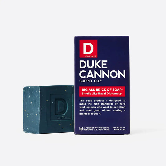 Large, dark green bar of soap with "D" logo and fresh, aquatic scent. Available in 10 oz size. Navy blue box labeled "Big Ass Brick of Soap - Naval Diplomacy - Plain Box.