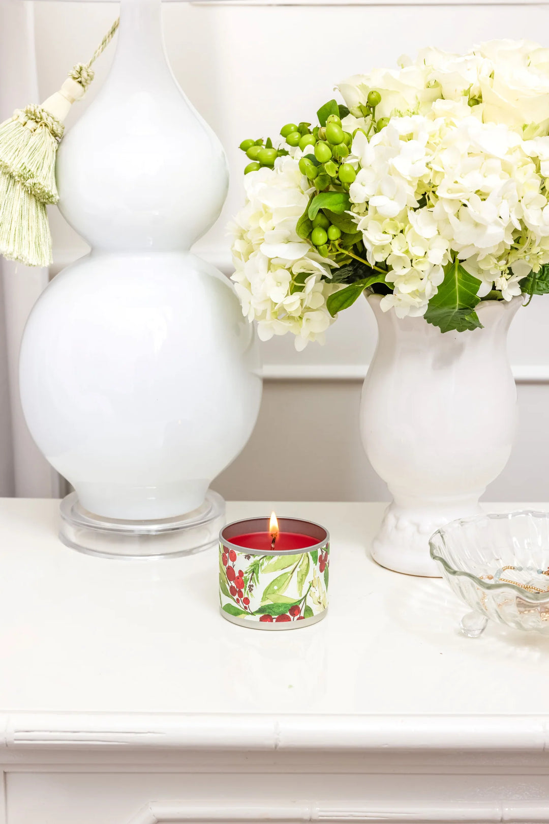 Lit Merry Memories 4oz tin candle with red wax, holiday botanical print, and ginger, cinnamon, and vanilla fragrance.
