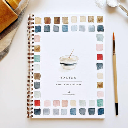The Baking watercolor workbook is a spiral-bound guide with baking-themed illustrations, colorful swatches along the edges, and a clearly labeled cover. Includes a paintbrush and step-by-step instructions. Available sizes not specified.