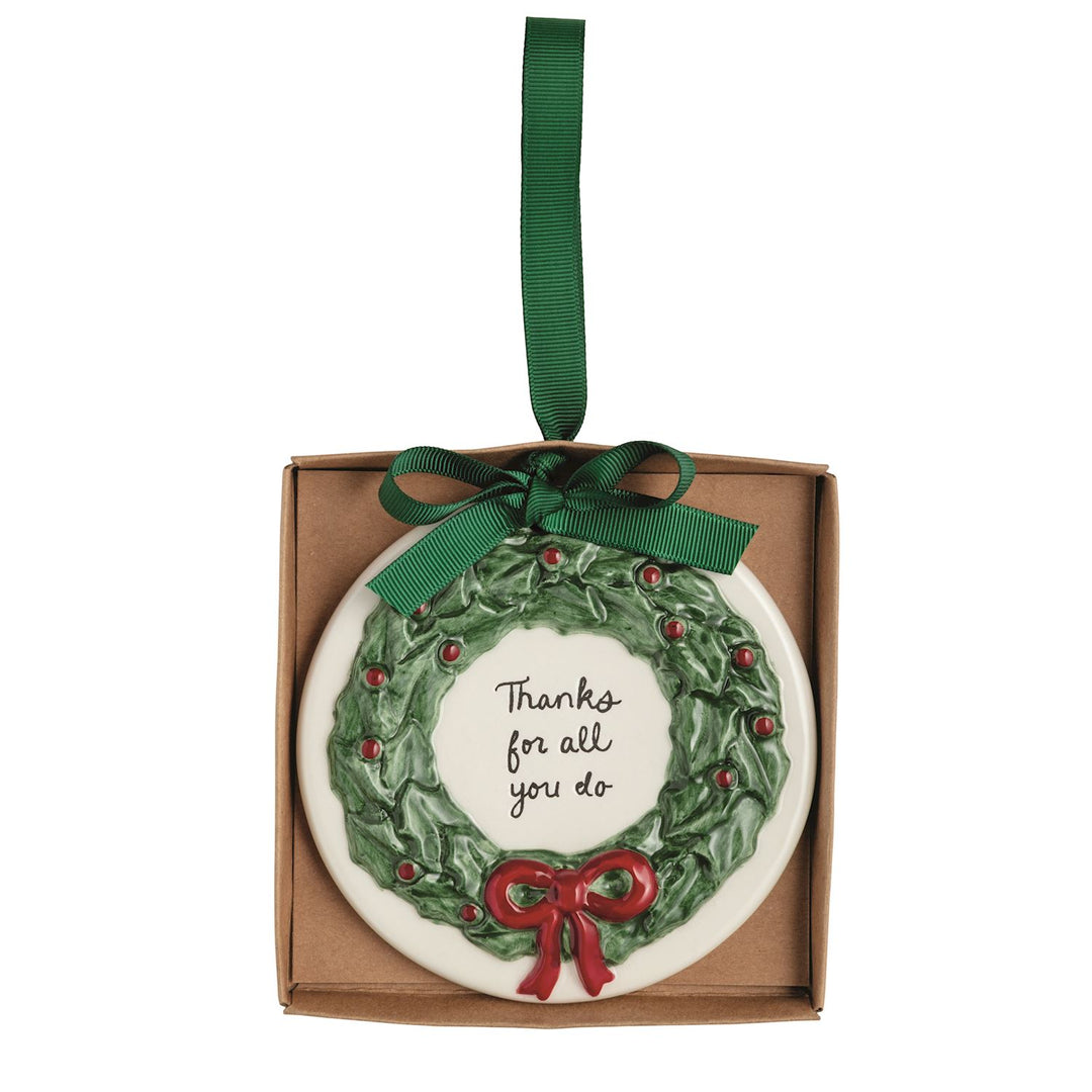 Round, hand-painted ceramic Thank You ornament featuring a holly wreath, a red bow, and the text “Thanks for all you do,” hanging from a green ribbon.