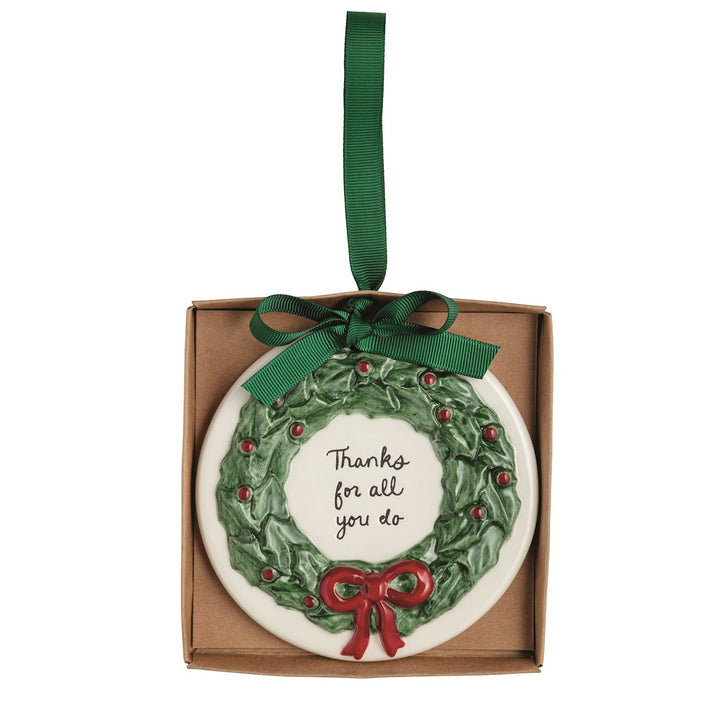 Round, hand-painted ceramic Thank You ornament featuring a holly wreath, a red bow, and the text “Thanks for all you do,” hanging from a green ribbon.