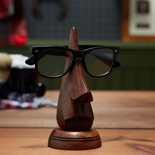 The Nose Eyeglass Holder in Gift Box displays black glasses on a nose-shaped stand. Available in small and large sizes.
