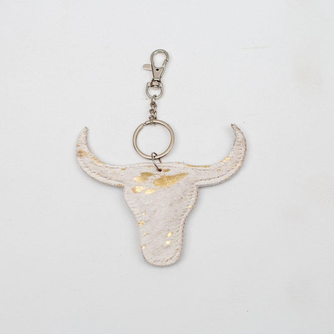 Bull skull-shaped keychain in white with gold flecks, metallic clasp. Sizes available. Unique leather bag accessory.