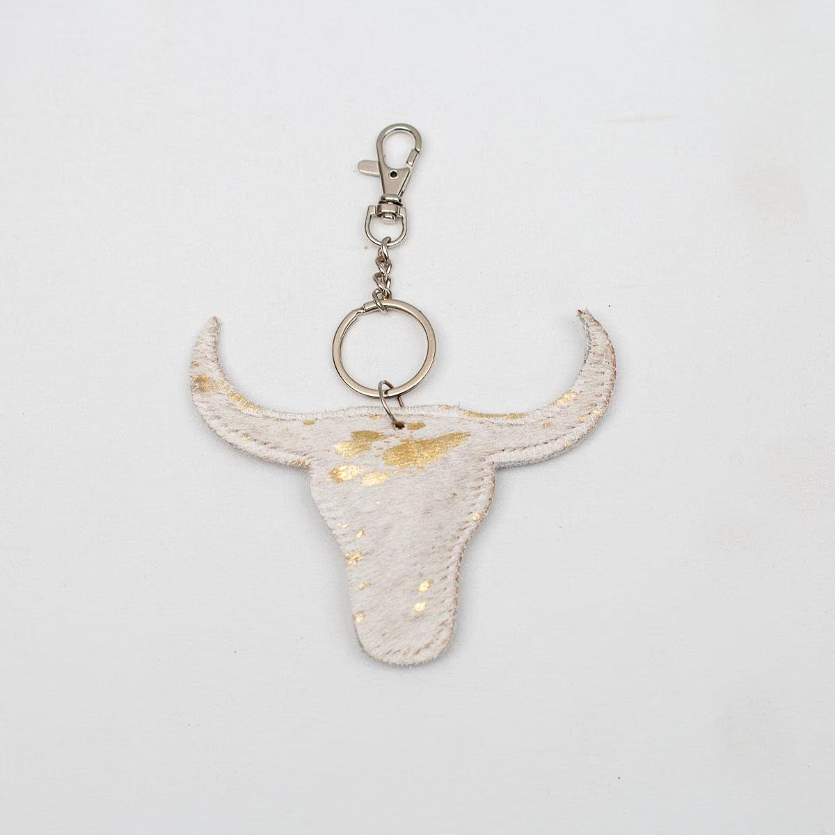 Bull skull-shaped keychain in white with gold flecks, metallic clasp. Sizes available. Unique leather bag accessory.