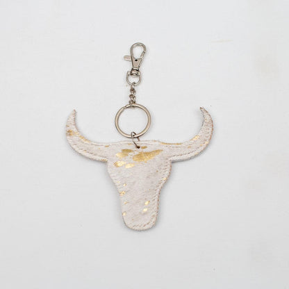Bull skull-shaped keychain in white with gold flecks, metallic clasp. Sizes available. Unique leather bag accessory.