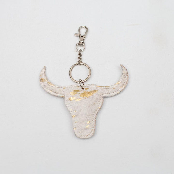 Bull skull-shaped keychain in white with gold flecks, metallic clasp. Sizes available. Unique leather bag accessory.