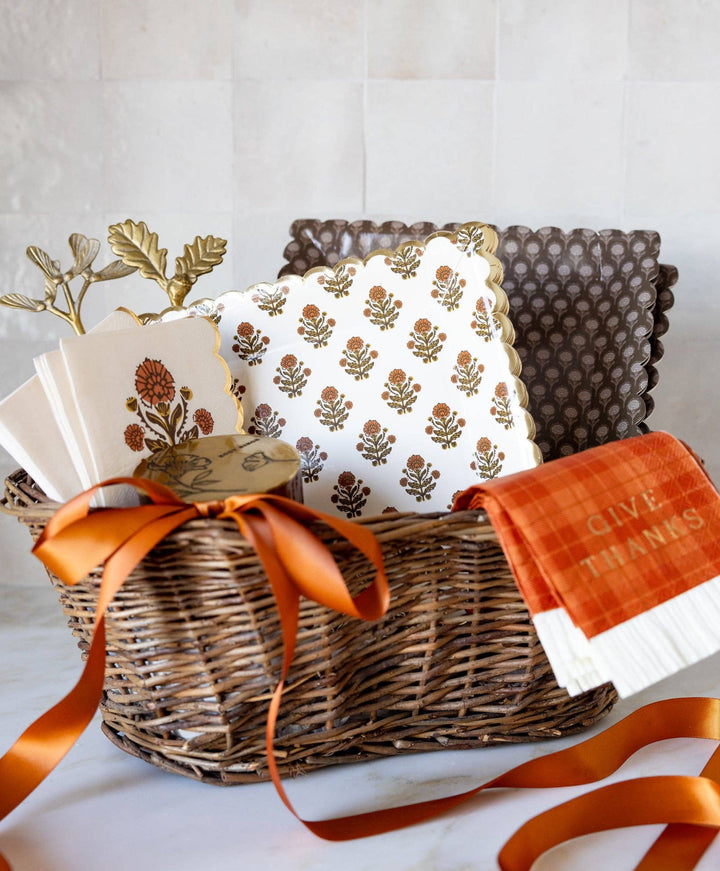 Thanksgiving Basket includes fall-themed napkins, “Give Thanks” towel, gold leaf decoration, brown quilted placemats, and an orange ribbon. Sizes available: Standard and Large.