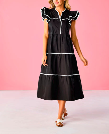 The Pia Ric Rac Midi Dress is an elegant black tiered dress with white trim and ruffled sleeves. Available sizes: XS, S, M, L, XL.