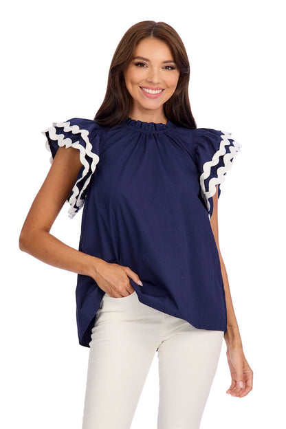 The Angie Ric Rac Top is a navy blue cotton poplin blouse featuring ruffled sleeves with white wave accents. Available sizes: XS, S, M, L, XL.
