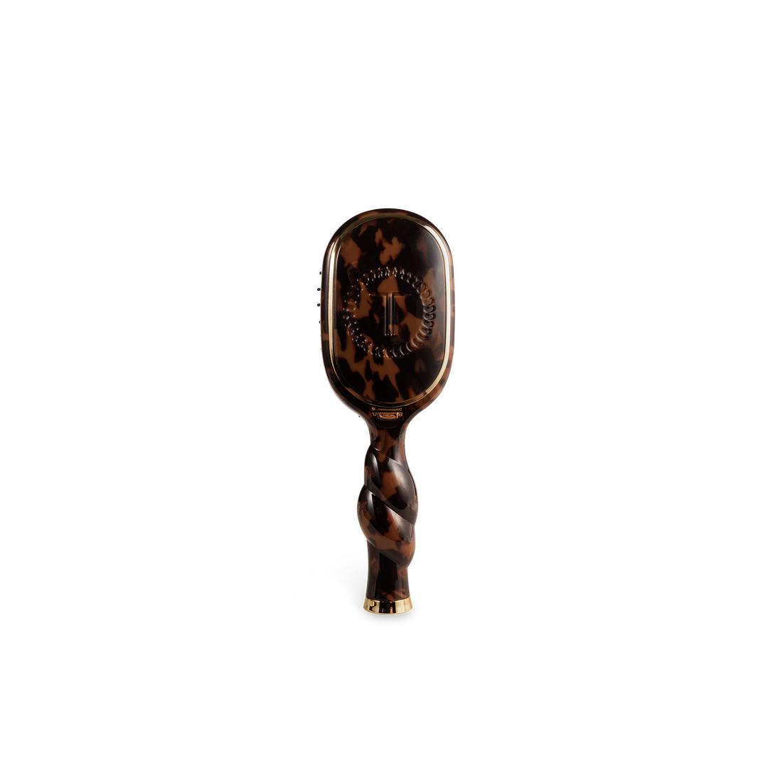 The Mini Boar Brush | Tortoise is a compact brown tortoiseshell boar bristle brush with a twisted handle and gold accents. Available in mini size.