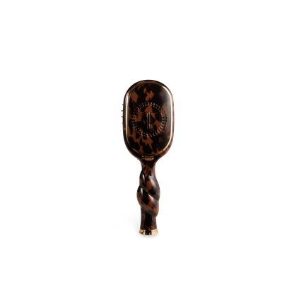 The Mini Boar Brush | Tortoise is a compact brown tortoiseshell boar bristle brush with a twisted handle and gold accents. Available in mini size.