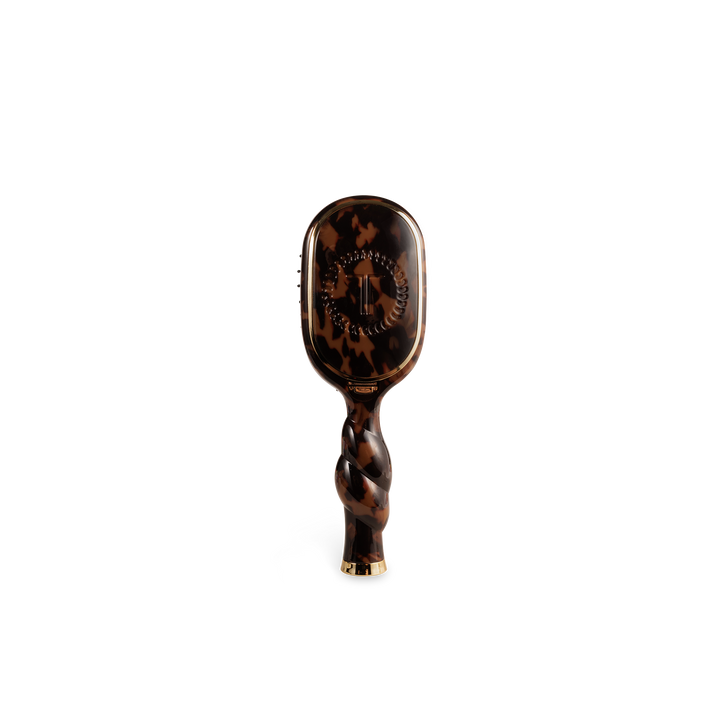 The Mini Boar Brush | Tortoise is a compact brown tortoiseshell boar bristle brush with a twisted handle and gold accents. Available in mini size.