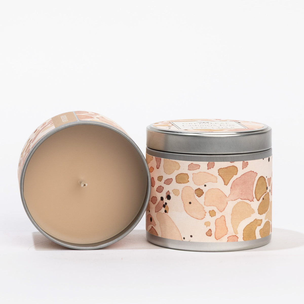 Two Cashmere Kiss Tin Candles, 4 oz. each, with abstract pink, beige, and brown labels; one closed, one open to show wax.