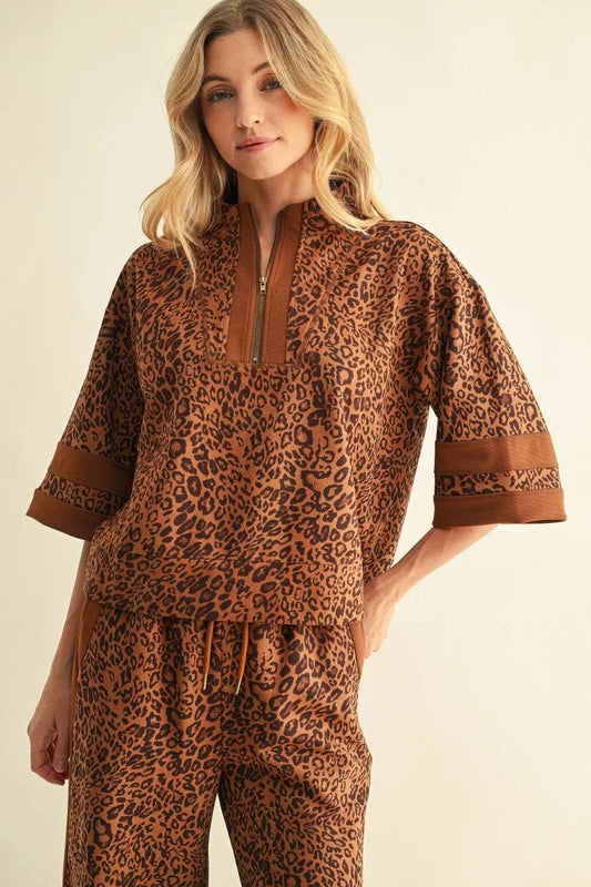 Leopard Zip-Up Top with half-zip collar, elbow-length sleeves, and decorative bands above the cuffs. Available in sizes XS–XL.