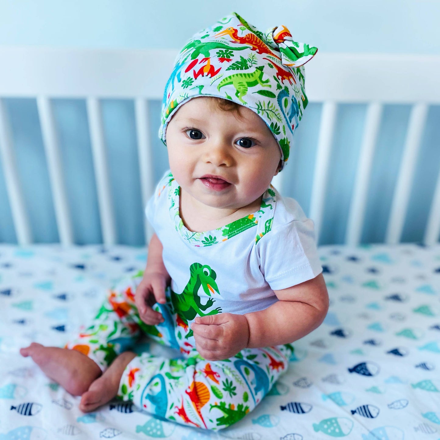 Baby modeling the set in a white crib in a blue room. Looking at something off in the distance.