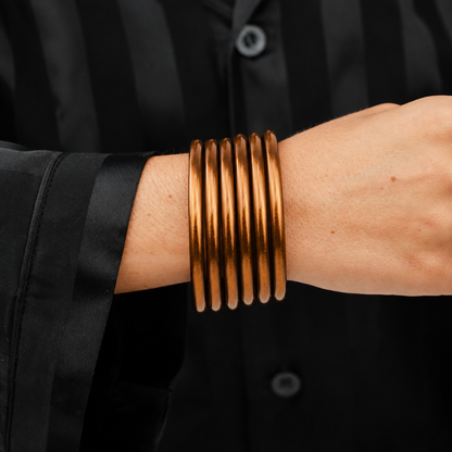 The Saddle All Weather Bangle, a thick handcrafted gold-toned bracelet, shown stacked; available in multiple sizes.
