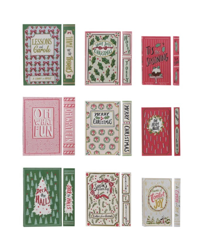 Six vintage-style canvas book storage boxes featuring festive titles: “Lessons and Carols,” “Holly Jolly Christmas,” “Tis the Seasoning,” “Oh What Fun,” “Merry Christmas,” and “Comfort and Joy.”.