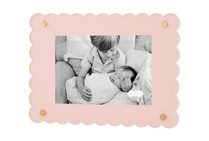 A black and white photo of a young boy gently touching a baby's head, both lying on a sofa, framed in a Scalloped Acrylic Frame with gold accents.