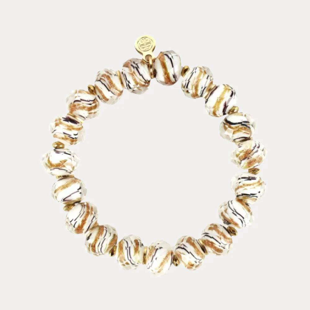 The Fjord Bracelet is a handcrafted Nordic piece with round wavy white beads streaked with brown and gold, small gold spacers, and a delicate gold charm. Available sizes: S, M, L.