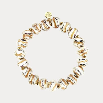 The Fjord Bracelet is a handcrafted Nordic piece with round wavy white beads streaked with brown and gold, small gold spacers, and a delicate gold charm. Available sizes: S, M, L.
