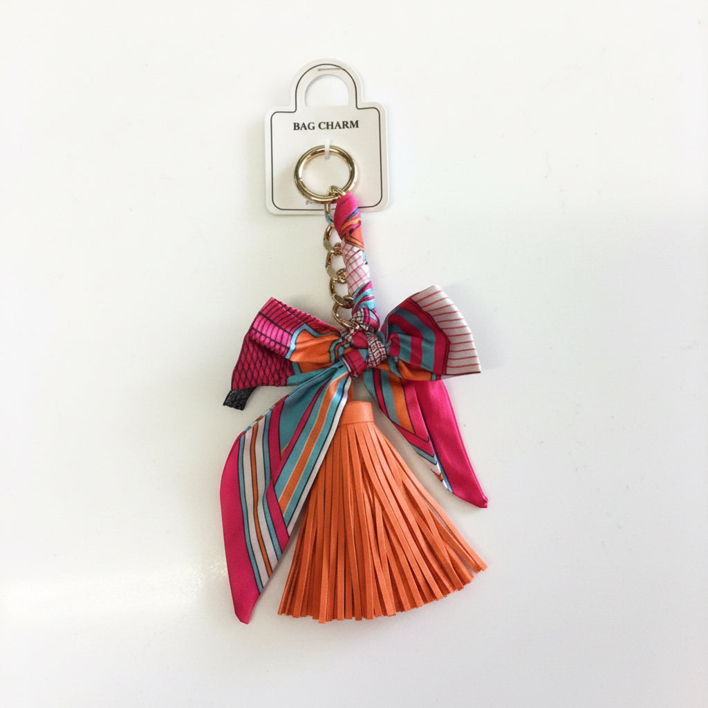 Gold keyring with pink and blue bow ribbon and orange leather tassel. Available in one size.